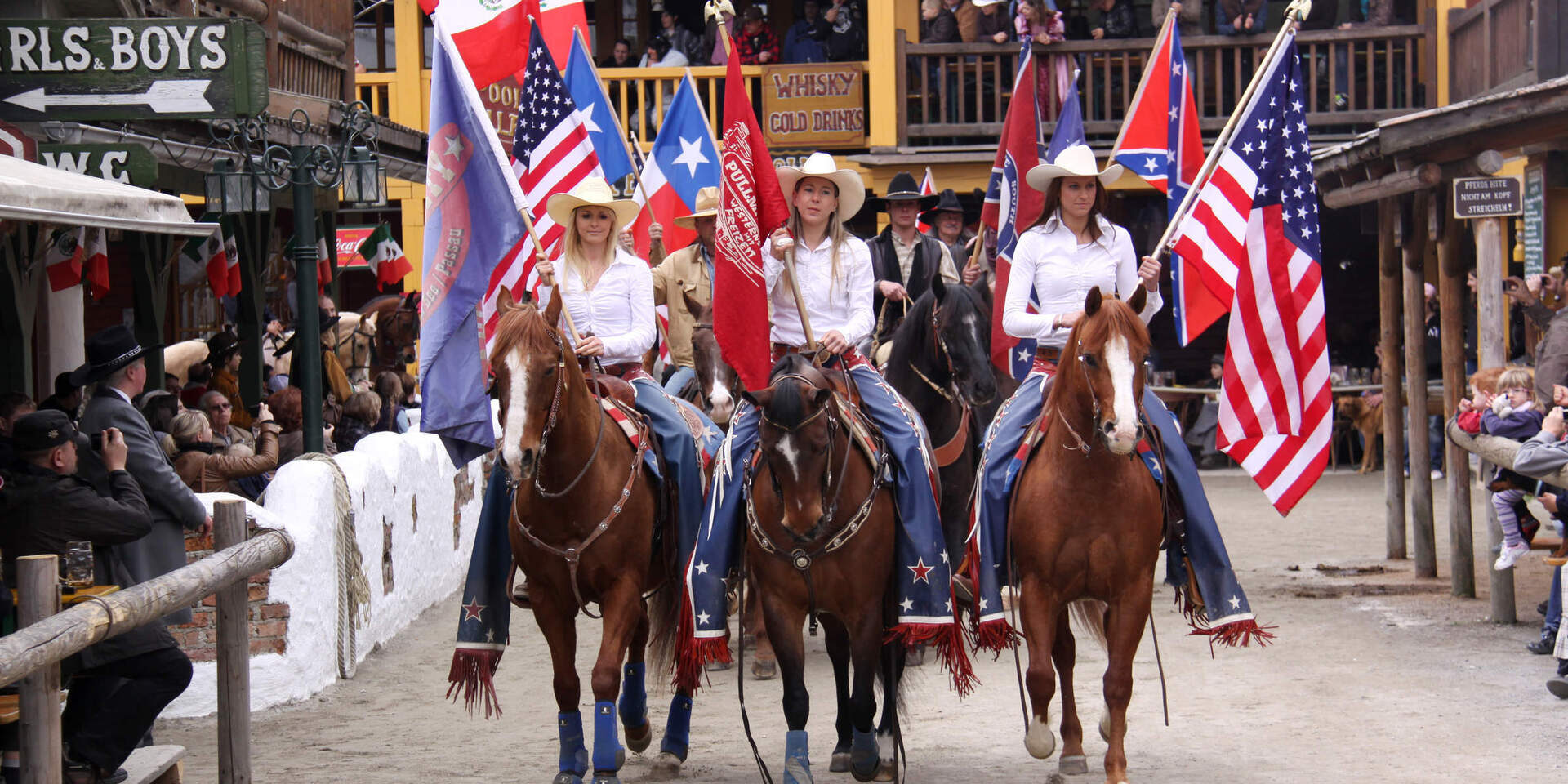 Eine Gruppe von Menschen reitet auf Pferden durch die Straßen von Pullman City Western town im Bayerischen Wald.